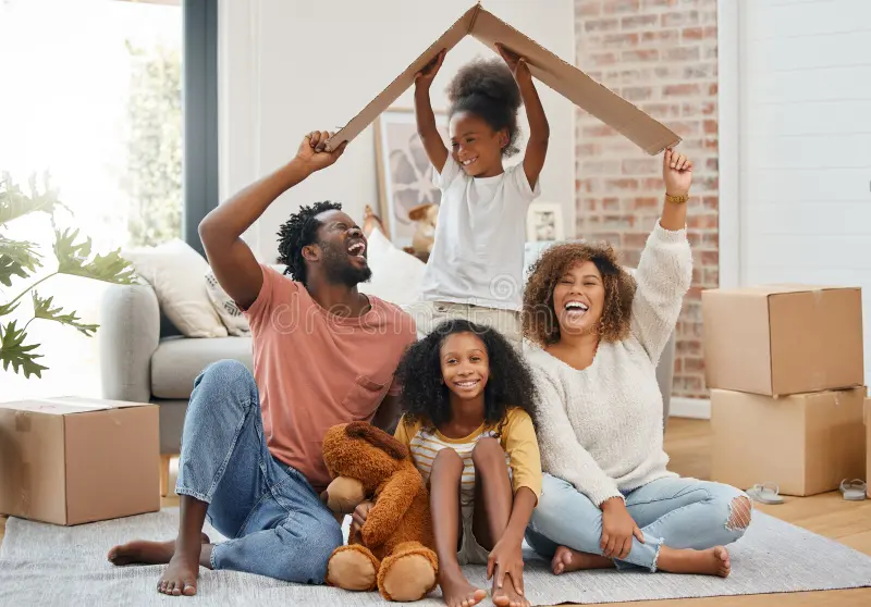 Happy family sitting together and forming a roof shape with cardboard while moving into a new home.